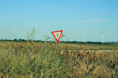Yield sign on the road. Red traffic sign Give Way with moving motorcycle and wind turbines on background with blue sky and wild grass.の写真素材