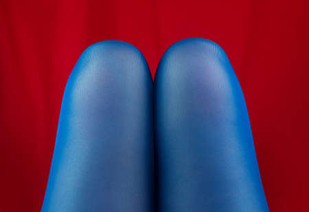 Female legs knees in blue tights on red fabric background. Spring autumn fashion collection modern style. Vivid vibrant contrasting colors.Fashionable advertising vertical banner Body positive conceptの写真素材