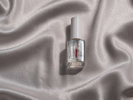 Nail polish bottle mockup with harsh shadow on white silk background french manicure cosmetics product. Sparkling transparent nailpolish against delamination cracking make-up. Design branding templateの写真素材