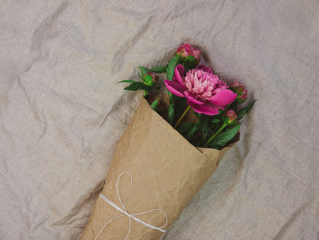 Pink peony flowers bouquet in kraft paper on gray linen fabric background top view, Minimal flat lay holidays celebrating concept.Women's Mother's Day birthday greeting card template mockup copy spaceの写真素材
