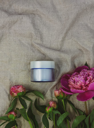 Blue glass cream jar mockup on lilnen fabric background fresh pink peony flower.Natural skincare...