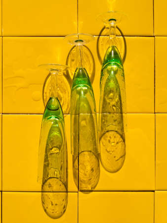 Wet crystal green glasses on yellow bar tile background with harsh shadow. Refreshing summer drinks. Cold natural gin vodka cocktail hot summer day. Non alcoholic soda clear water tonic Party vacationの写真素材