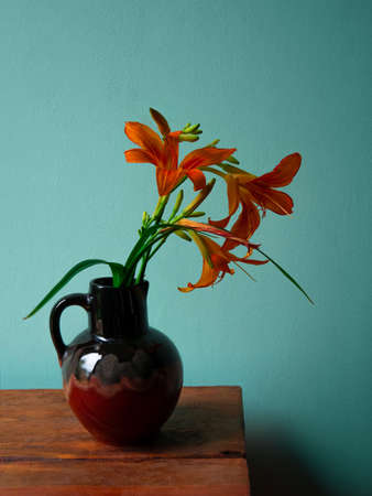 Tiger lily in ceramic vase with shadow turquoise wall background. Lilium lancifolium orange flowers bouquet on wooden farmhouse table. Summer cottagecore aesthetic country rural minimalism dark style.の写真素材