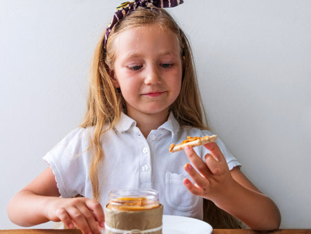 Child eating crispbread with peanut butter sitting at table home kitchen. School girl with bread slice wholegrain snack sandwich. Organic nutritious vegetarian superfood meal vegan healthy lifestyle.の写真素材