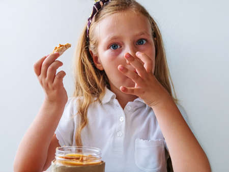 Child eating crispbread with peanut butter sitting at table home kitchen. School girl with bread slice wholegrain snack sandwich. Organic nutritious vegetarian superfood meal vegan healthy lifestyle.の写真素材