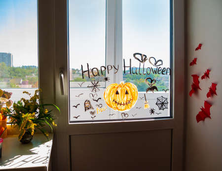 Child painting pumpkin on window preparing celebrate Halloween. Little kid draws decorates room interior with paper bats celebration autumn holiday at home Creative family leisure lockdown new realityの写真素材