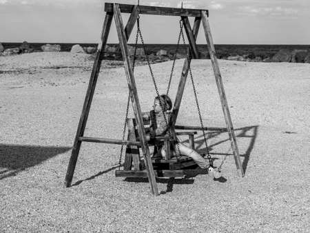 Little girl chilling resting on wooden beach swing. Happy child relaxing enjoying life sun. Lifestyle autumn travel real people outdoor.Fall spring vacation Freedom happiness adventure Black and whiteの写真素材