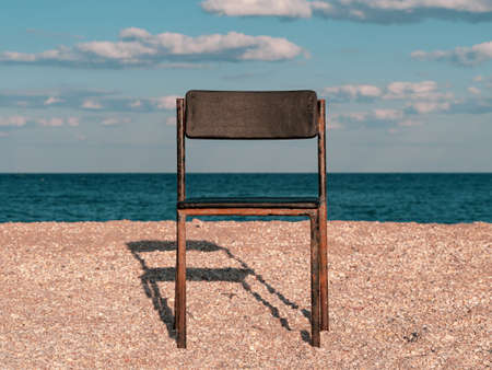 Black beach chair on empty sand beach with blue sea water background. Minimalism style autumn travel relaxation, spring fall vacation. No people, nobody, introversion psychology melancholia depressionの写真素材