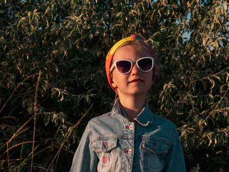 Happy little girl portrait on green leaves background. Kid walking alone on autumn sea shore. Pretty child in sunglasses resting on sand beach. Travel vacation Freedom lifestyle happiness concept.の写真素材