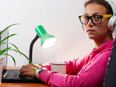 Female freelancer in headphones laptop Work from home, distance e-learning office. Pretty student girl drinking coffee listening video conference talking online. Business woman in eyeglasses at desk.の写真素材