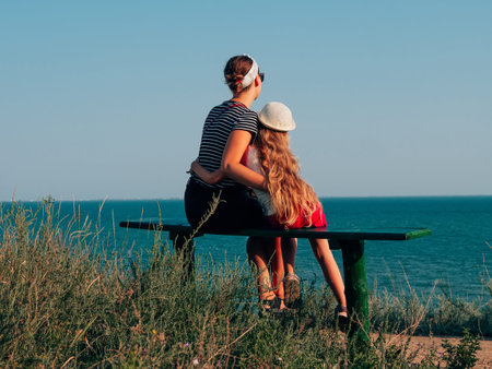 Happy mother and daughter sitting on bench on marine landscape back view. Mom and child having fun walking together looking at the sea from above.Lifestyle real people. Happiness family travel conceptの写真素材