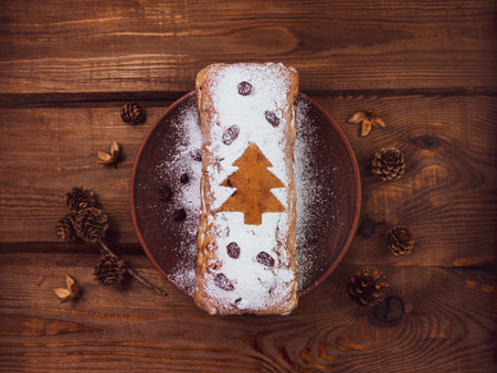 Christmas fruitcake with powdered sugar tangerine cranberry fir tree festive decoration wooden background flat lay. Stollen cake loaf Wholegrain flour dough baking recipe rustic holiday table top viewの写真素材