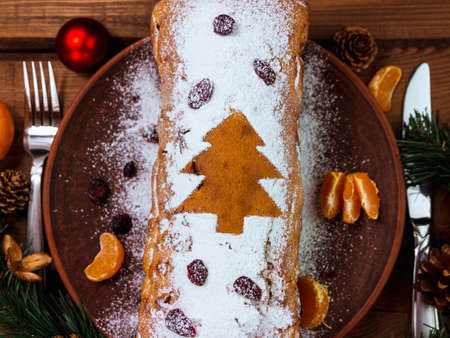 Christmas fruitcake with powdered sugar tangerine cranberry fir tree festive decoration wooden background flat lay. Stollen cake loaf Wholegrain flour dough baking recipe rustic holiday table top viewの写真素材