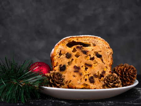 Christmas fruitcake powdered sugar on white plate dark background seasonal decorations. Xmas...