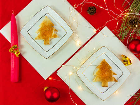 Christmas table setting toast on white plate silverware candle on red tablecloth background flat lay. New year festive party restaurant dinner decoration Winter Holiday Greeting card invitation designの写真素材