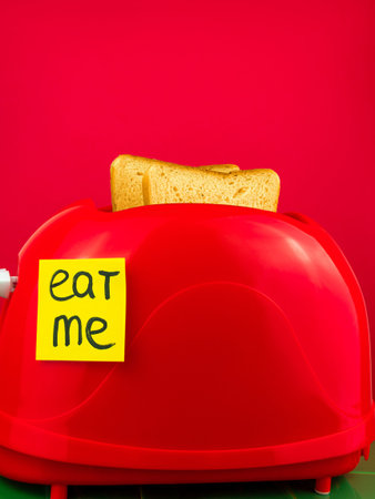 Red toaster with crispy fresh bread slices on green tile kitchen. Morning toasts breakfast idea creative minimalism concept. Eat Me yellow sticker minimal style composition. Colorful food background.の写真素材