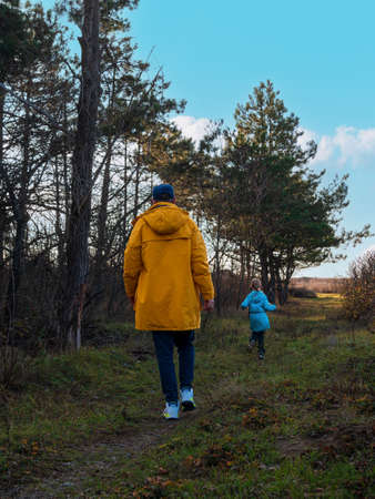 Travelers father and daughter walking together in pine forest enjoying scenic landscape blue cloudy sky back view. Active Lifestyle nature tourism. Family local travel hiking trail journey Backpackingの写真素材