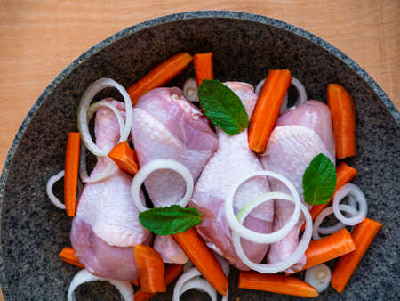 Raw chicken drumsticks with carrots, onions and green herbs in frying pan top view. Fresh meat vegetables salad spices cooking. Homemade healthy yummy food ingredient background copy space flat lay.の写真素材