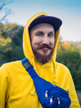 Red bearded millennial man with mustache in yellow hoody smiling portrait closeup Backpacker hiking climbing Carpathian Mountains forest scenic view.Travel Lifestyle wanderlust into the wild adventureの写真素材