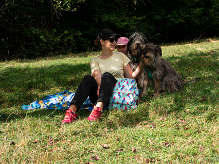 Happy family mother with daughter and two dogs sitting on green grass lawn having fun picnic spending time together hiking in the mountains. People and pets outdoors lifestyle photo candid emotions.の写真素材