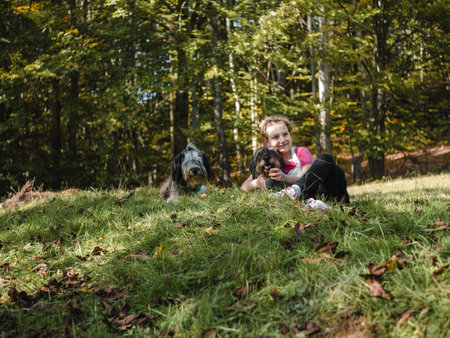 Happy little girl with two dogs sitting on a green grass lawn having fun, family picnics, spending time together, hiking in the mountains. People and pets outdoors lifestyle photo candid emotions.の写真素材