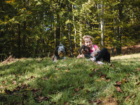 Happy little girl with two dogs sitting on a green grass lawn having fun, family picnics, spending time together, hiking in the mountains. People and pets outdoors lifestyle photo candid emotions.の写真素材