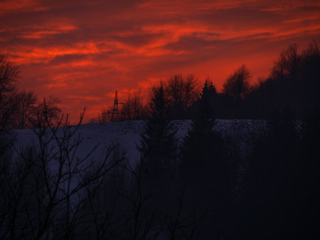 Sunset in the mountains with orange red sky and clouds. Winter Carpathian Mountains view cloudscape. Pine fir tree forest in Carpathians Scenic wood landscape Village in Transcarpathia Ukraine, Europeの写真素材