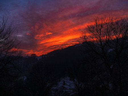 Sunset in the mountains with orange red sky and clouds. Winter Carpathian Mountains view cloudscape. Pine fir tree forest in Carpathians Scenic wood landscape Village in Transcarpathia Ukraine, Europeの写真素材