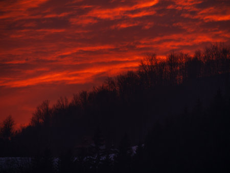Sunset in the mountains with orange red sky and clouds. Winter Carpathian Mountains view cloudscape. Pine fir tree forest in Carpathians Scenic wood landscape Village in Transcarpathia Ukraine, Europeの写真素材