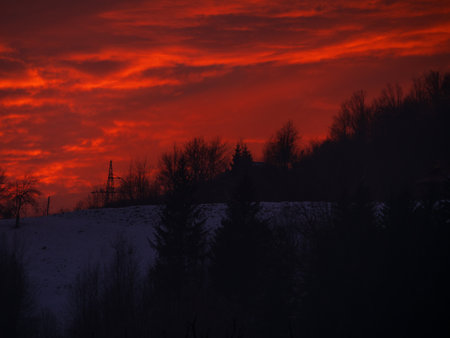 Sunset in the mountains with orange red sky and clouds. Winter Carpathian Mountains view cloudscape. Pine fir tree forest in Carpathians Scenic wood landscape Village in Transcarpathia Ukraine, Europeの写真素材