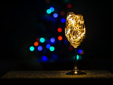 Crystal wine glasses with golden glowing garland on Christmas table bokeh light background. Festive screensaver. Romantic New Years eve dinner champagne couple in love.Magic winter holidays atmosphereの写真素材