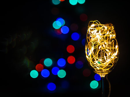 Crystal wine glasses with golden glowing garland on Christmas table bokeh light background. Festive screensaver. Romantic New Years eve dinner champagne couple in love.Magic winter holidays atmosphereの写真素材