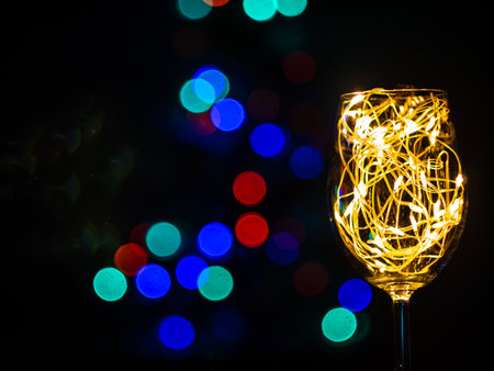 Crystal wine glasses with golden glowing garland on Christmas table bokeh light background. Festive screensaver. Romantic New Years eve dinner champagne couple in love.Magic winter holidays atmosphereの写真素材