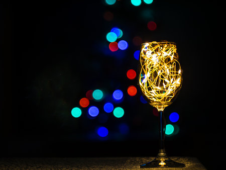 Crystal wine glasses with golden glowing garland on Christmas table bokeh light background. Festive screensaver. Romantic New Years eve dinner champagne couple in love.Magic winter holidays atmosphereの写真素材