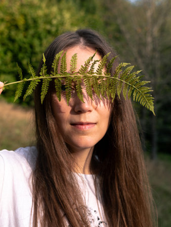 Portrait of a happy young woman with a fern leaf in her hand on mountain forest background. Autumn...