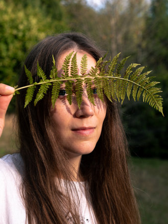 Portrait of a happy young woman with a fern leaf in her hand on mountain forest background. Autumn woods Natural beauty No makeup Haircare. Organic cosmetics concept Eco healthy herbal greenの写真素材