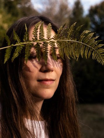 Portrait of a happy young woman with a fern leaf in her hand on mountain forest background. Autumn woods Natural beauty No makeup Haircare. Organic cosmetics concept Eco healthy herbal greenの写真素材