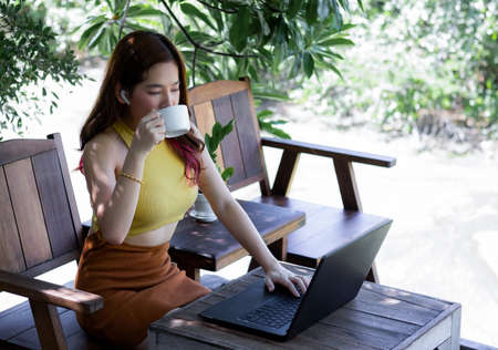 Young business woman work from home and drink coffee. Fresh atmosphere in the middle of nature. Work with computers and communicate via high speed internet. Social distancing in modern times.の写真素材