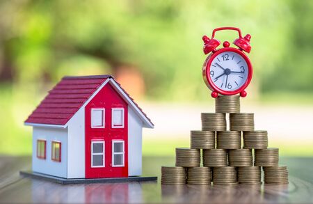 Red roof house And there are coins stacked with a red alarm clock placed on the pile of coins.Financial investment accounting concept Business risk starts with obstacles.Planning to buy a house.の写真素材