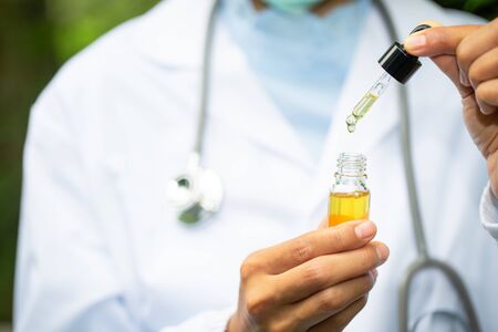 Glass bottle handle, CBD hemp oil. Doctors or researchers hold a bottle of hemp oil. Background with medical stethoscope.medical marijuana concept, CBD cannabis OIL. hemp product, close upの写真素材