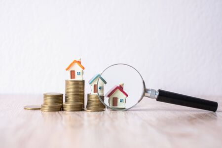 A magnifying glass that is being placed near the house on a pile of coins. Search for houses, investment ideas, real estate. Small houses have space to enter text.の写真素材
