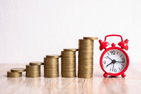 A red alarm clock and a pile of coins resting on the table. Ideas to save money, ideas for business...