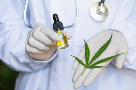 Glass bottle handle, CBD hemp oil. Doctors or researchers hold a bottle of hemp oil. Background with medical stethoscope.medical marijuana concept, CBD cannabis OIL. hemp product, close upの写真素材