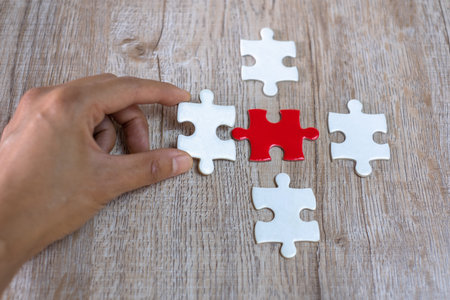 The human hand catches the white puzzle Pieces of red and white puzzle on a brown background....