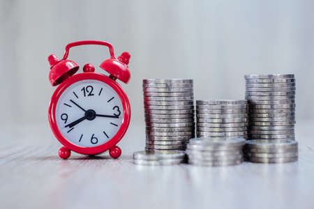 A red alarm clock and a pile of coins resting on the table. Ideas to save money, ideas for business growth, use the right time to invest, the idea of using time to be worth the money. Investment risk.の写真素材