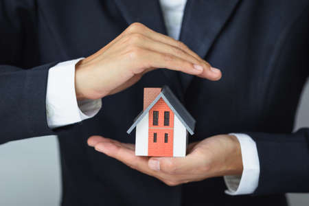 A house model in the hands of a businessman To protect home protection concept using real estate investor's gestures and symbols, custody of credit and contracts. After-sales service.の写真素材