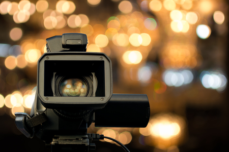 Front view of video camera with light reflection in lens and bokeh light in background. Selective focus.の写真素材