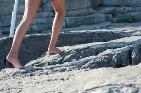 The girl goes barefoot on the rocks, climbing up.の写真素材