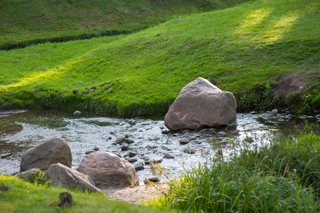Stones in the river interfere with the flow of water, the lawn by the river.の写真素材