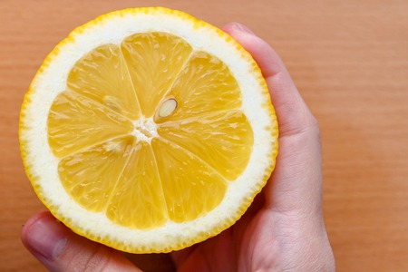 A woman's hand takes a slice of organic fresh yellow lemon on a wooden cutting board. Slices of lemon on a board on a green background. View from above. Lemon in hand on brown backgroundの写真素材
